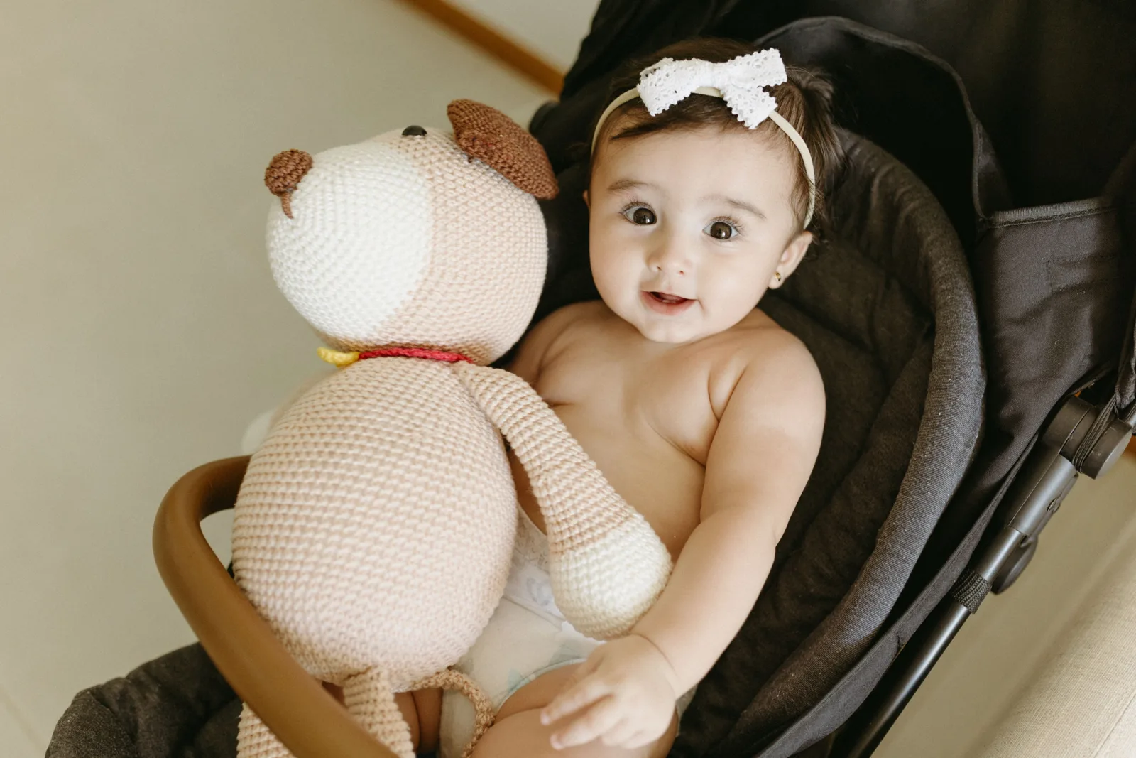 Un bébé installé dans sa poussette tient une peluche au crochet