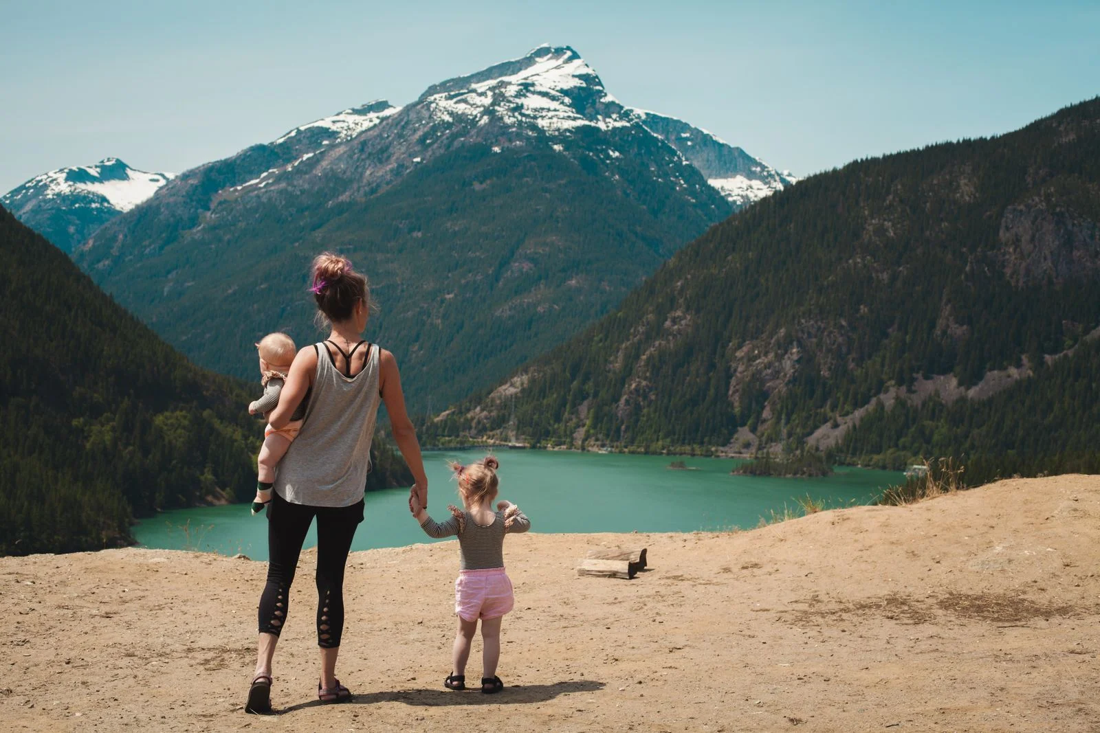 Une mère, son bébé dans les bras, et sa fille marchent vers un lac de montagne